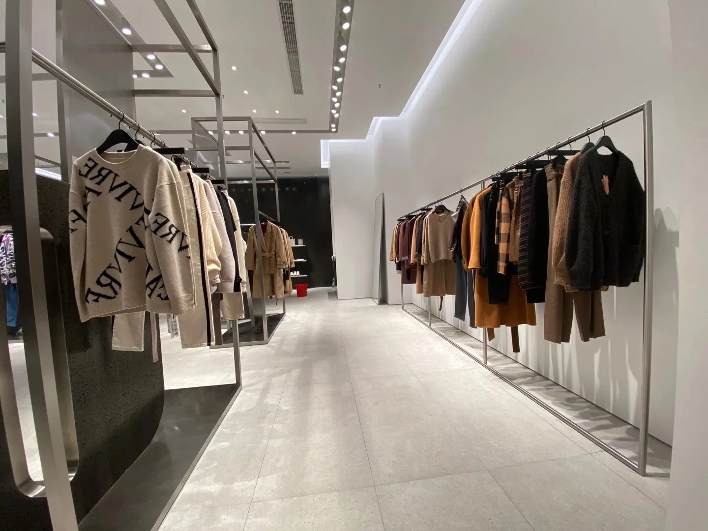 Modern fashion store aisle with recessed downlights and track lighting.